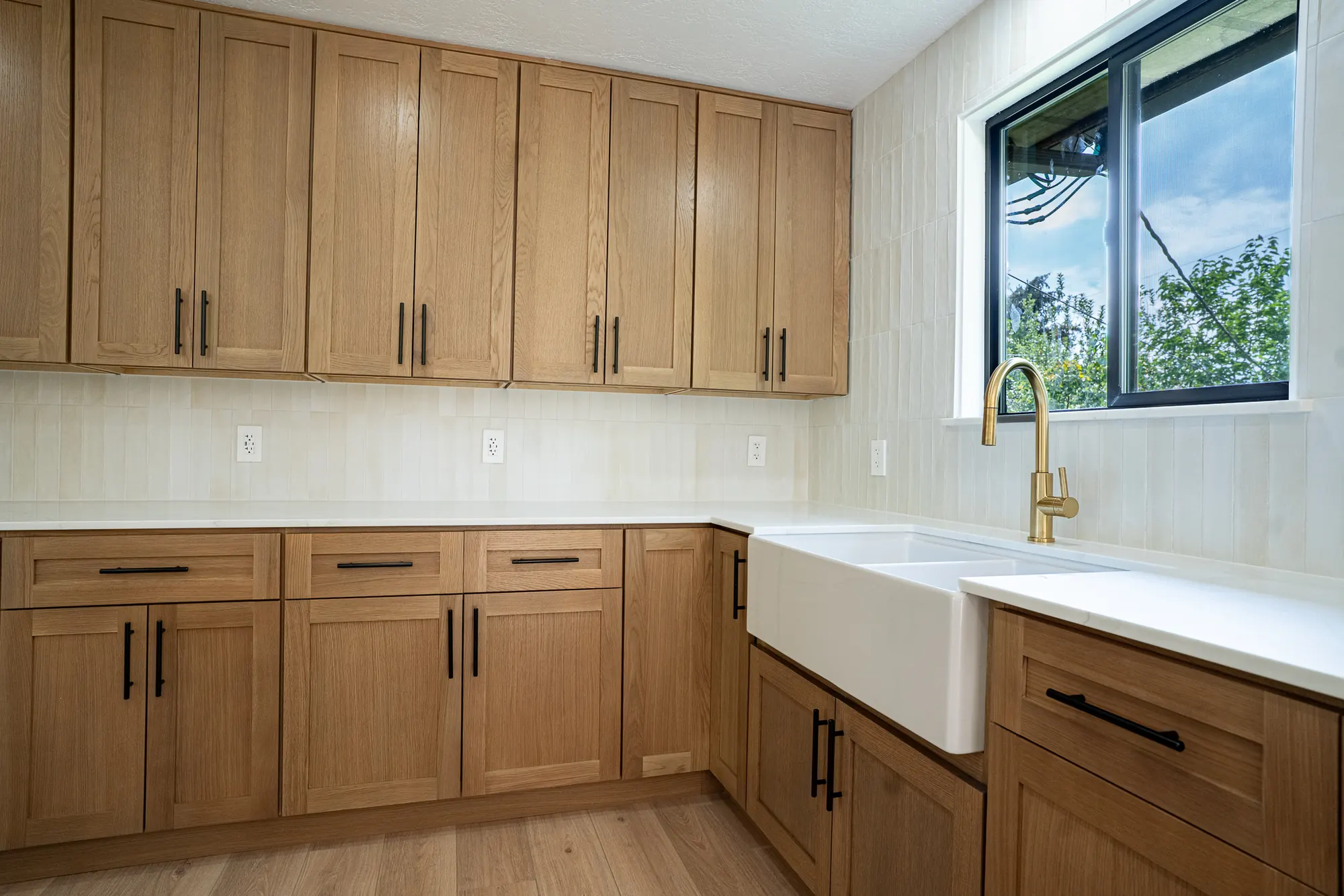 White oak kitchen with black pulls, quartz counters, a farmhouse sink, and cream stacked tile
